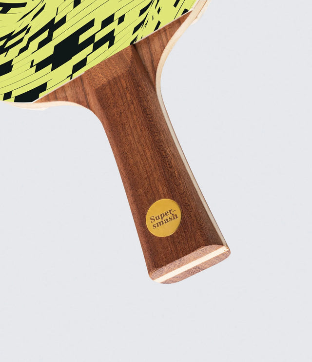 Close-up of a wooden ping pong paddle with a checkered yellow and black design on a light gray background.