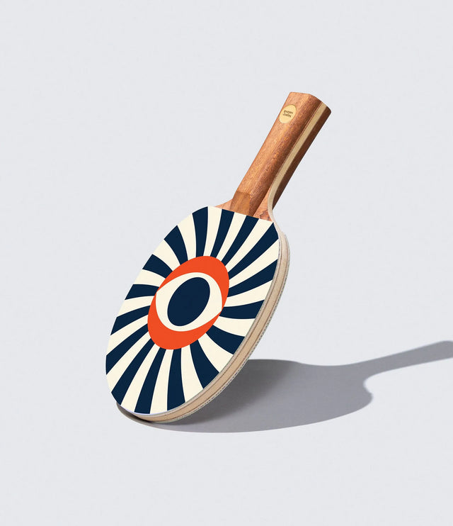 Ping pong paddle with a sunburst pattern on a light gray background